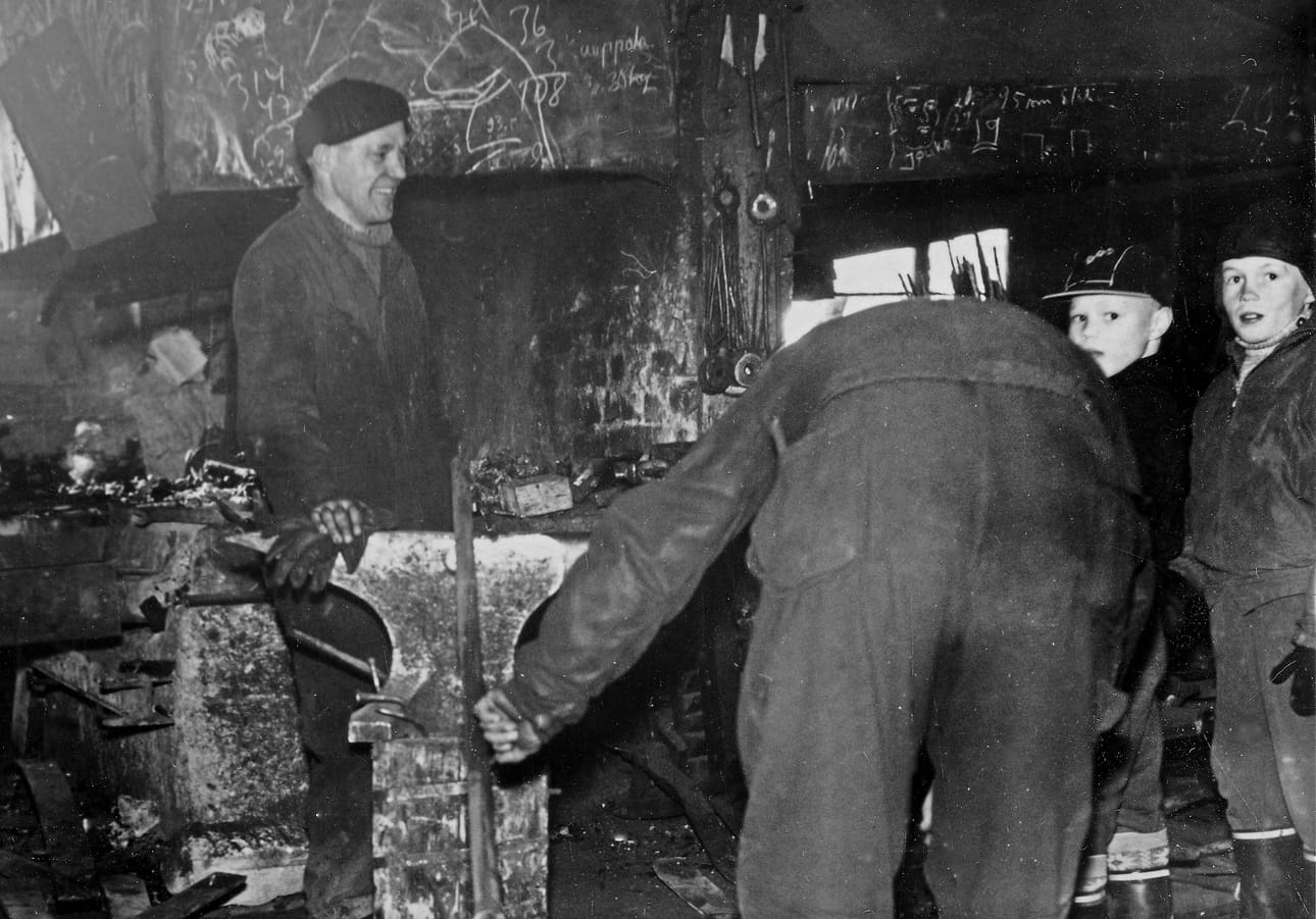 Seppä Toivo Heiskari (vas.) pajassaan, seuranaan oma poika Timo Heiskari ja siskonpoika Erkki Kervinen . Selin olevaa henkilöä ei ole tunnistettu.