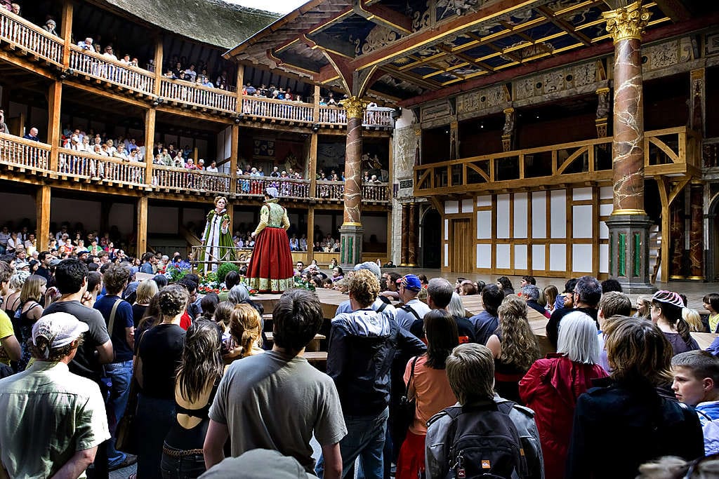 Globe-teatterin näyttämö on auki kolmelta sivulta. Yleisö istuu ympyrän muotoon rakennetuilla parvekkeilla puupenkeillä tai seisoo alhaalla lähellä näyttämöä.