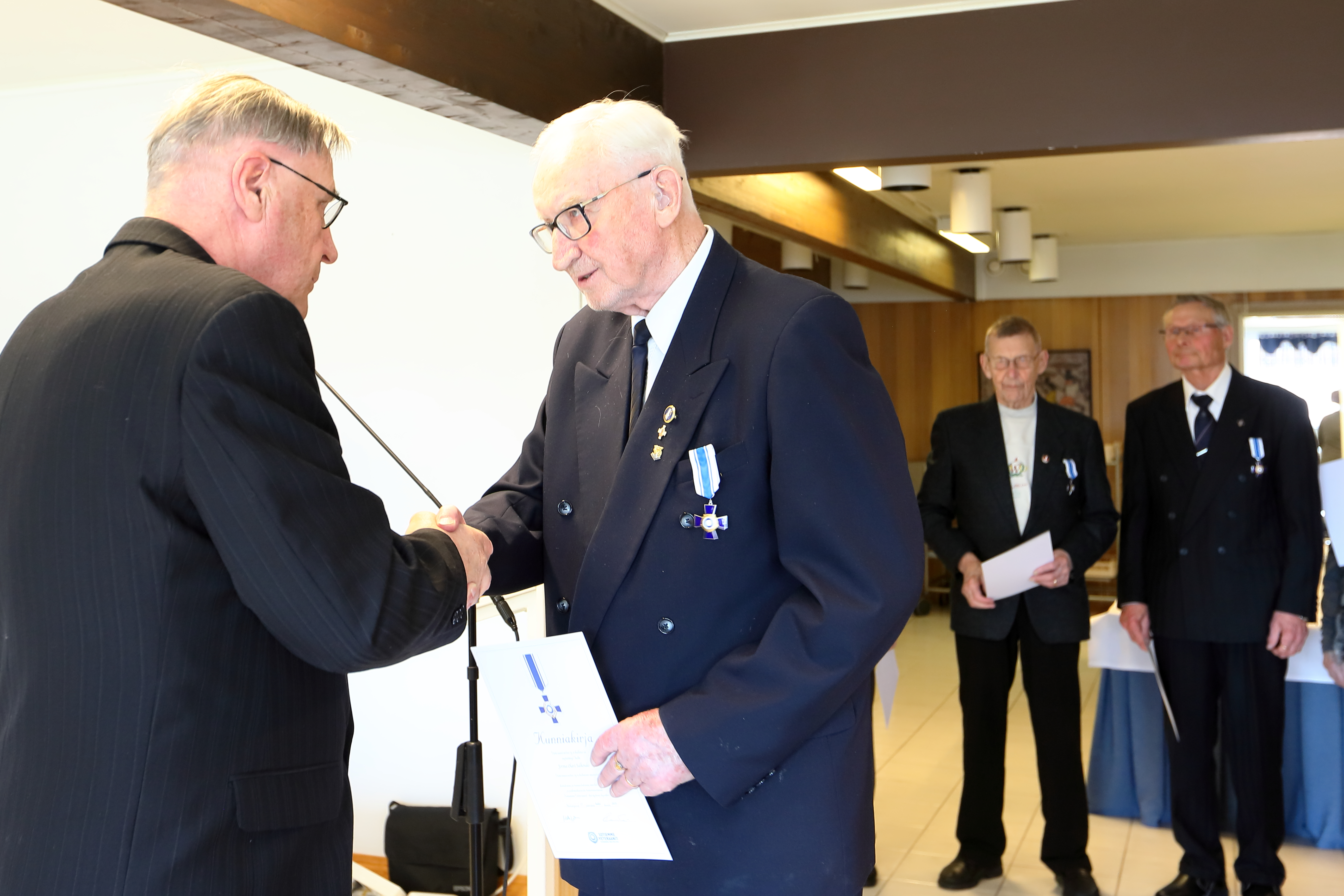 Erik Vuokila antaa Jorma Salkokarille Sotaveteraaniliiton kultaristin. Taustalla saman ristin saaneet Veikko Ranta-Eskola ja Unto Suomalainen.