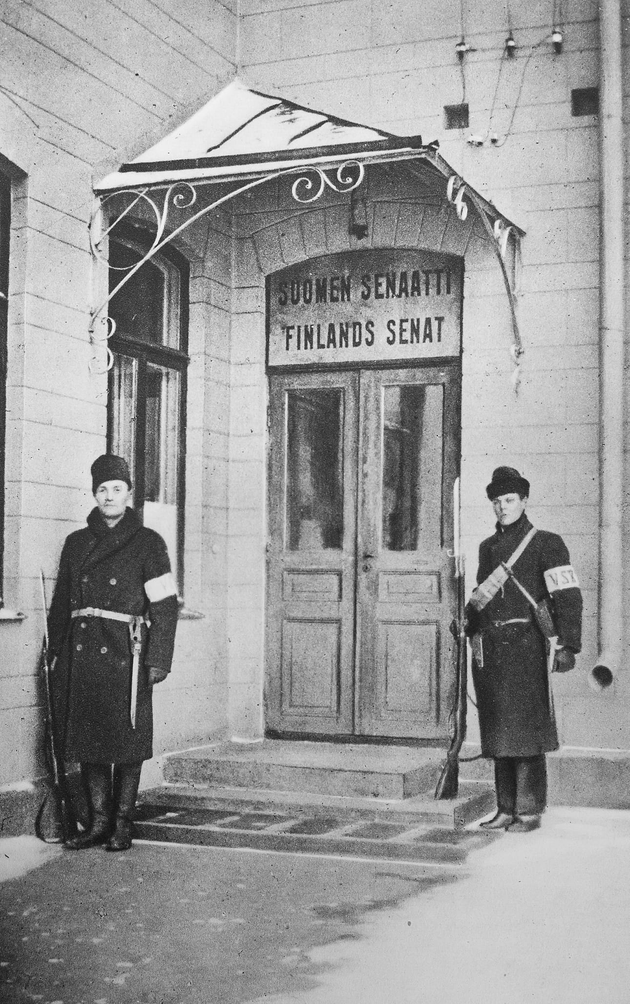 Suojeluskuntalaiset vartioivat ovella senaatin istuessa maaherrantalolla talvella 1918. Nimikilpi oli faneerilevyä.