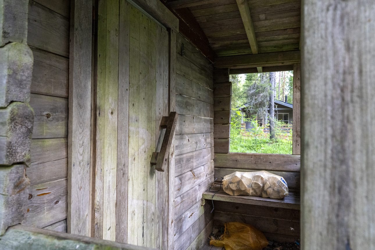 Saunan ovi ei ole lukossa. Kiukaan lämmitystä varten pitää ainakin toistaiseksi tuoda omat polttopuut. Saunan kuistilta näkyy autiotuvalle.