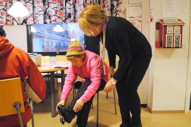 Eila Mäkelä veti liukuesteet kenkiensä päälle Maarit Säntin opastuksella. KUVAT: EEVA-LIISA KULJU