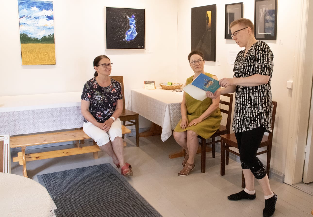 Rantsila-seuran Airi Juntunen ja Tuula Makkonen kuuntelivat, kun Eija Tuomaala luki Rantsila Kotiseutumme kirjasta, milloin Rantsila-seura on perustettu. Taustalla Taru Vähäsöyringin tauluja.
