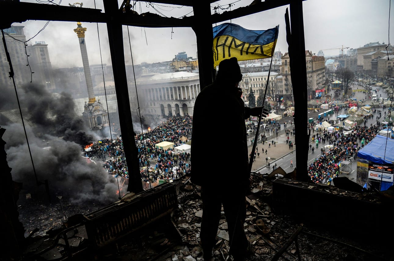 Mielenosoittaja piteli Ukrainan lippua palaneessa rakennuksessa Itsenäisyyden aukion laidalla Kiovassa helmikuussa 2014. LEHTIKUVA/AFP