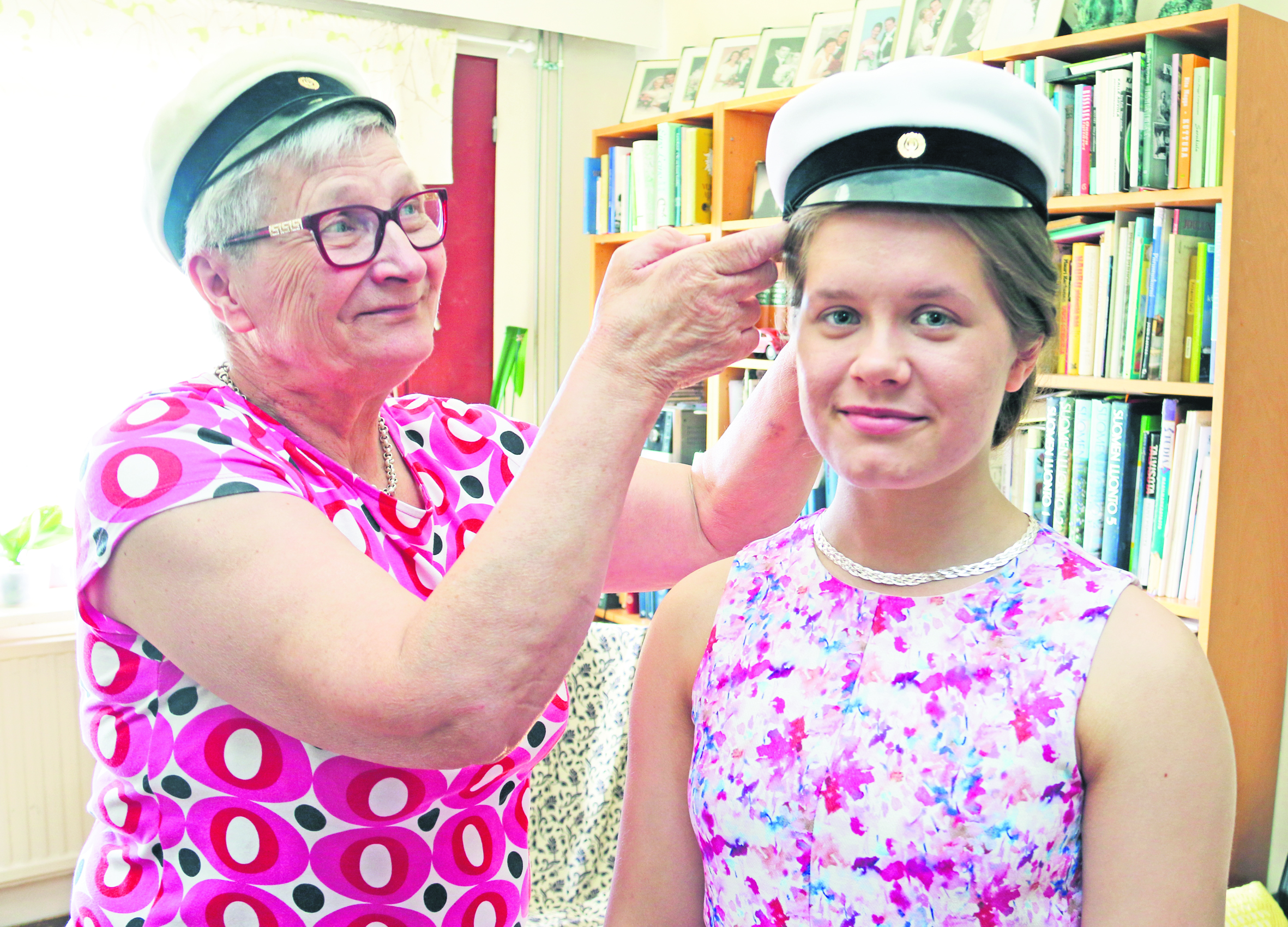 Maija Ahola testaa ylioppilakkia pojantyttärensä Jenniina Aholan päähän. Oman lakkinsa hän painoi kutreilleen 50 vuotta sitten.