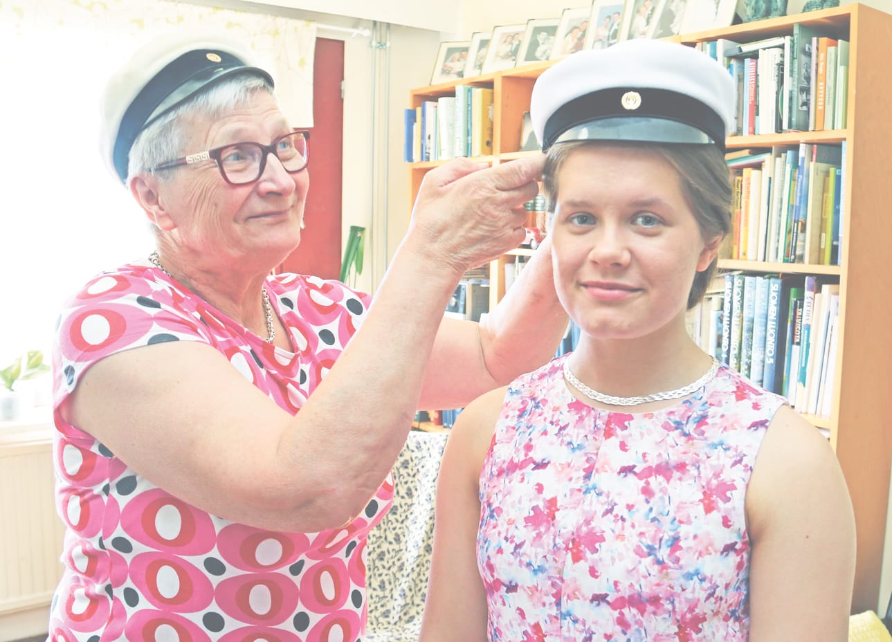 Maija Ahola testaa ylioppilakkia pojantyttärensä Jenniina Aholan päähän. Oman lakkinsa hän painoi kutreilleen 50 vuotta sitten.