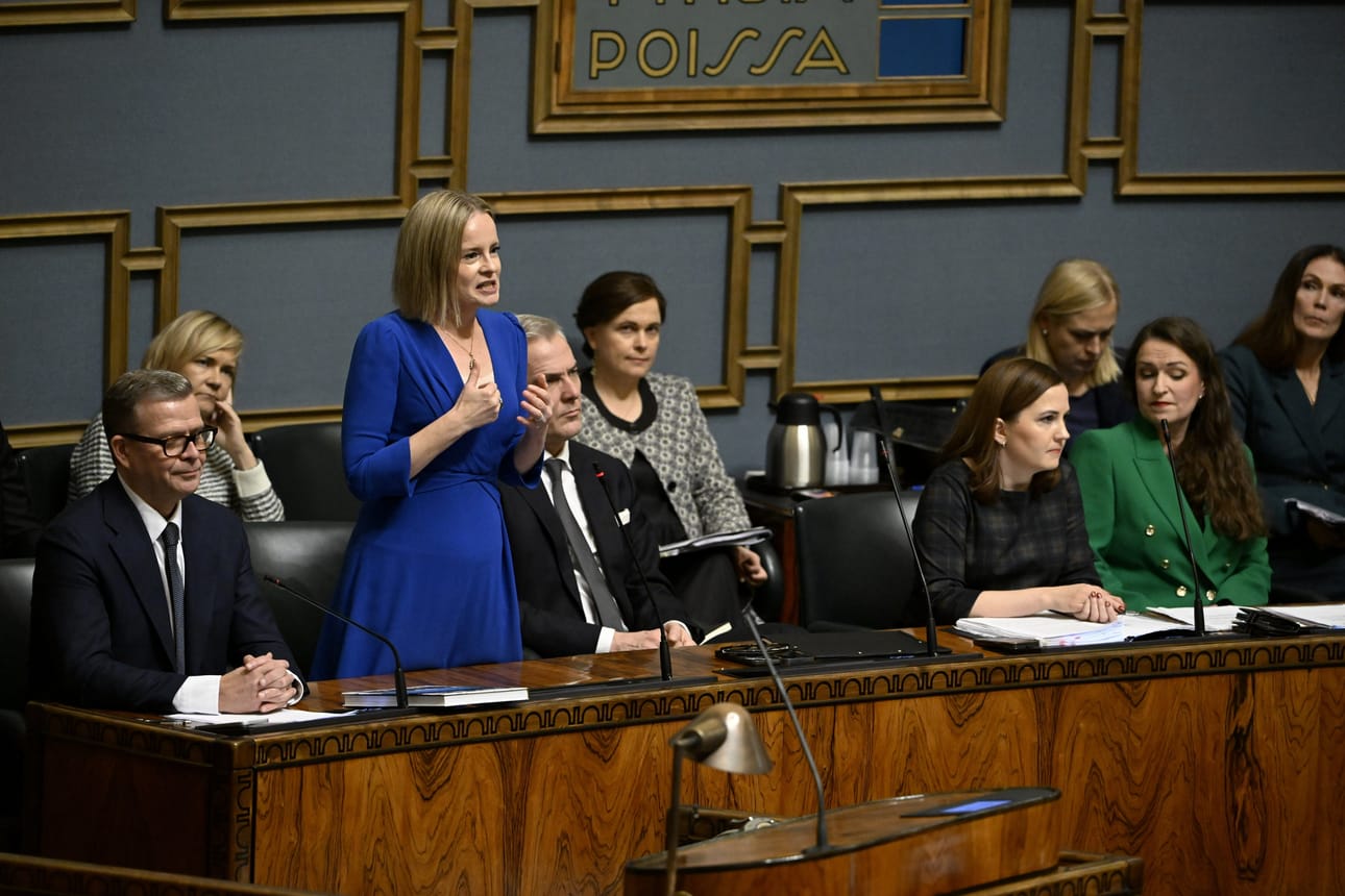 Valtiovarainministeri Riikka Purra vastausvuorossa eduskunnan suullisella kyselytunnilla Helsingissä 6. marraskuuta 2025, ympärillä pääministeri Petteri Orpo (vas.) ja ministerit Mari Rantanen, Anders Adlercreutz, Mari-Leena Talvitie, Sanni Grahn-Laasonen, Elina Valtonen, Anna-Kaisa Ikonen ja Lulu Ranne.