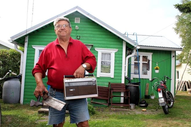 Egil Högbacka esittelee tuhopoltoista säästyneitä kolmea esinettä Leppäsalmen talon pihassa. Jäljelle jäivät vanha matkaradio, saha ja kirves. KUVA: LOTTA KALLIO
