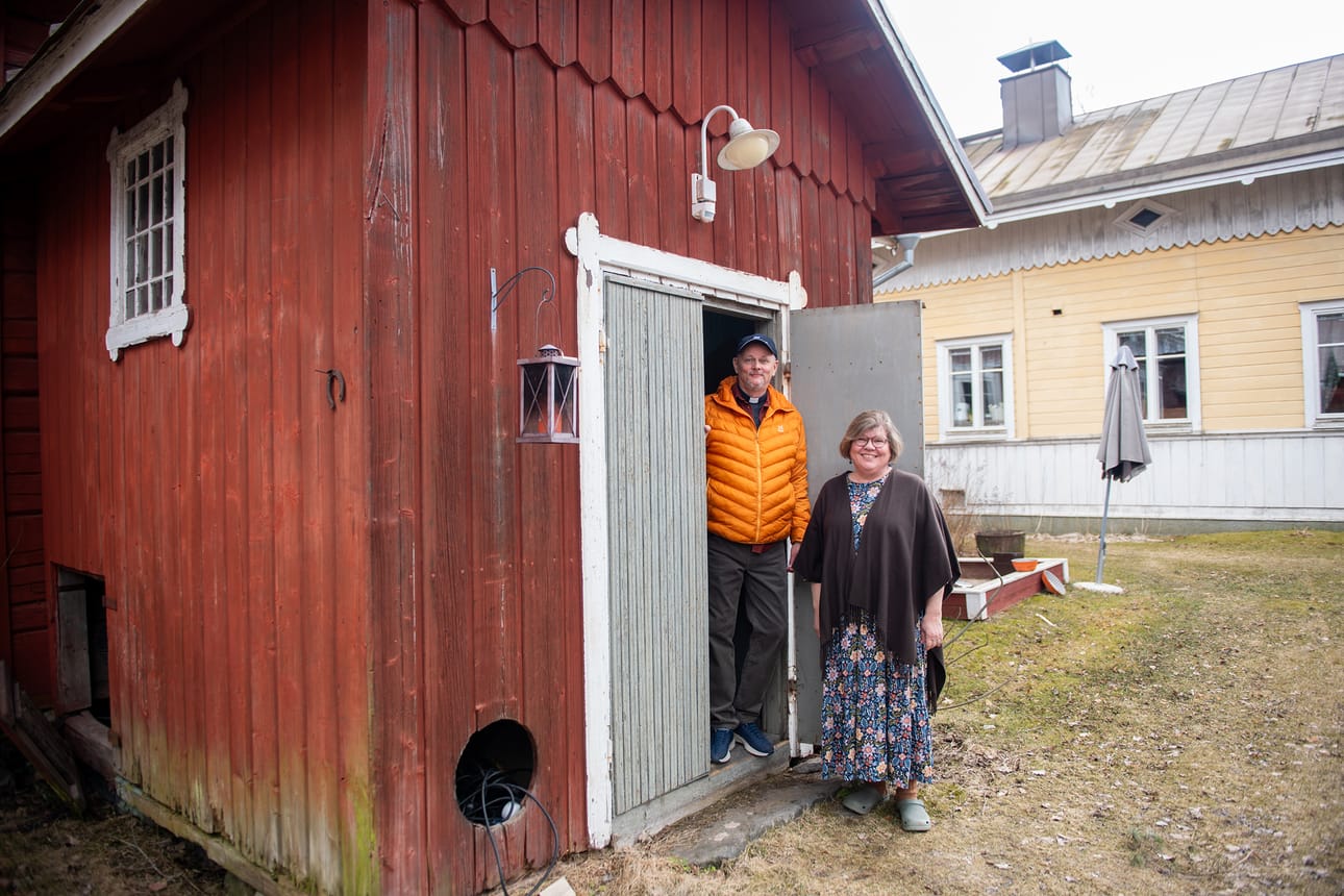 Pasi ja Anu Salminen seisovat rengintuvan ovella. Takana näkyy pappilan päärakennus, joka on nähnyt seitsemän kirkkoherran kaudet yli 130 vuoden aikana.