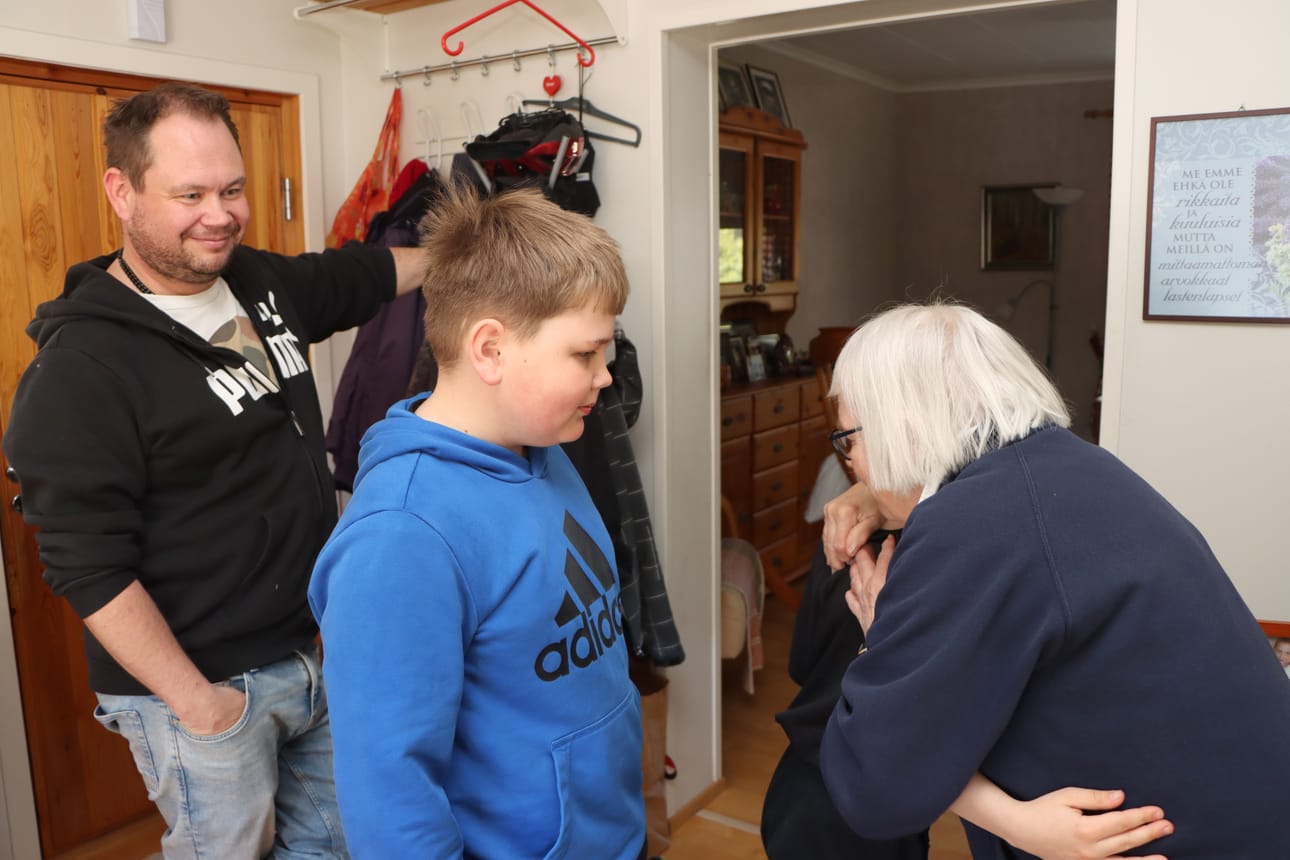 Niilo Wörlund antaa mummilleen Kirtsi Häkkiselle onnitteluhalauksen Kunniaisoäiti-reliefin saamisesta. Jonossa on Jone Sjöblom takanaan isänsä Jouko Sjöblom, Häkkisen poika.