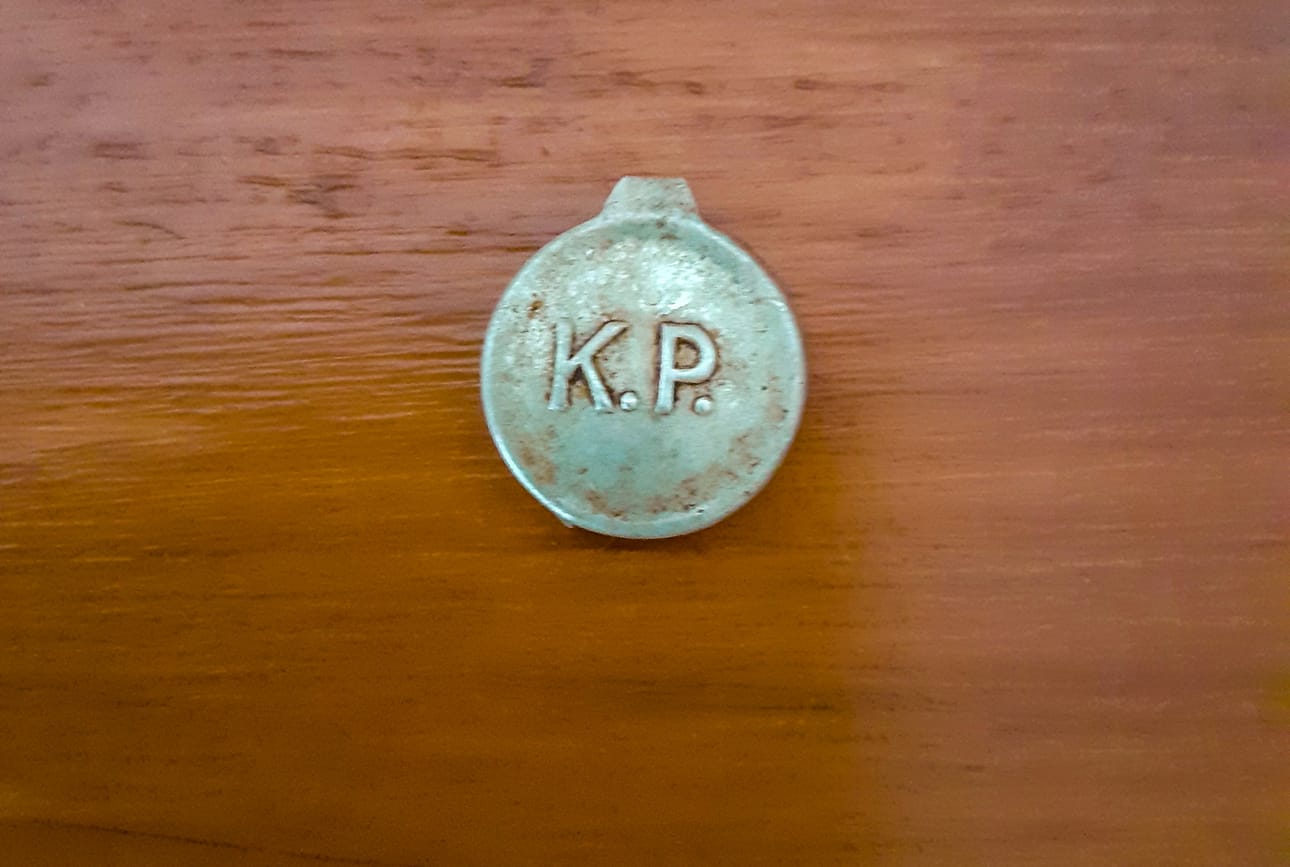 Toisella puolen lukee "K. P." Esineen tässä puolikkaassa on toisella puolen jonkinlainen lovi, jossa on Rauhalan arvion mukaan voinut olla esimerkiksi naru tai lanka.