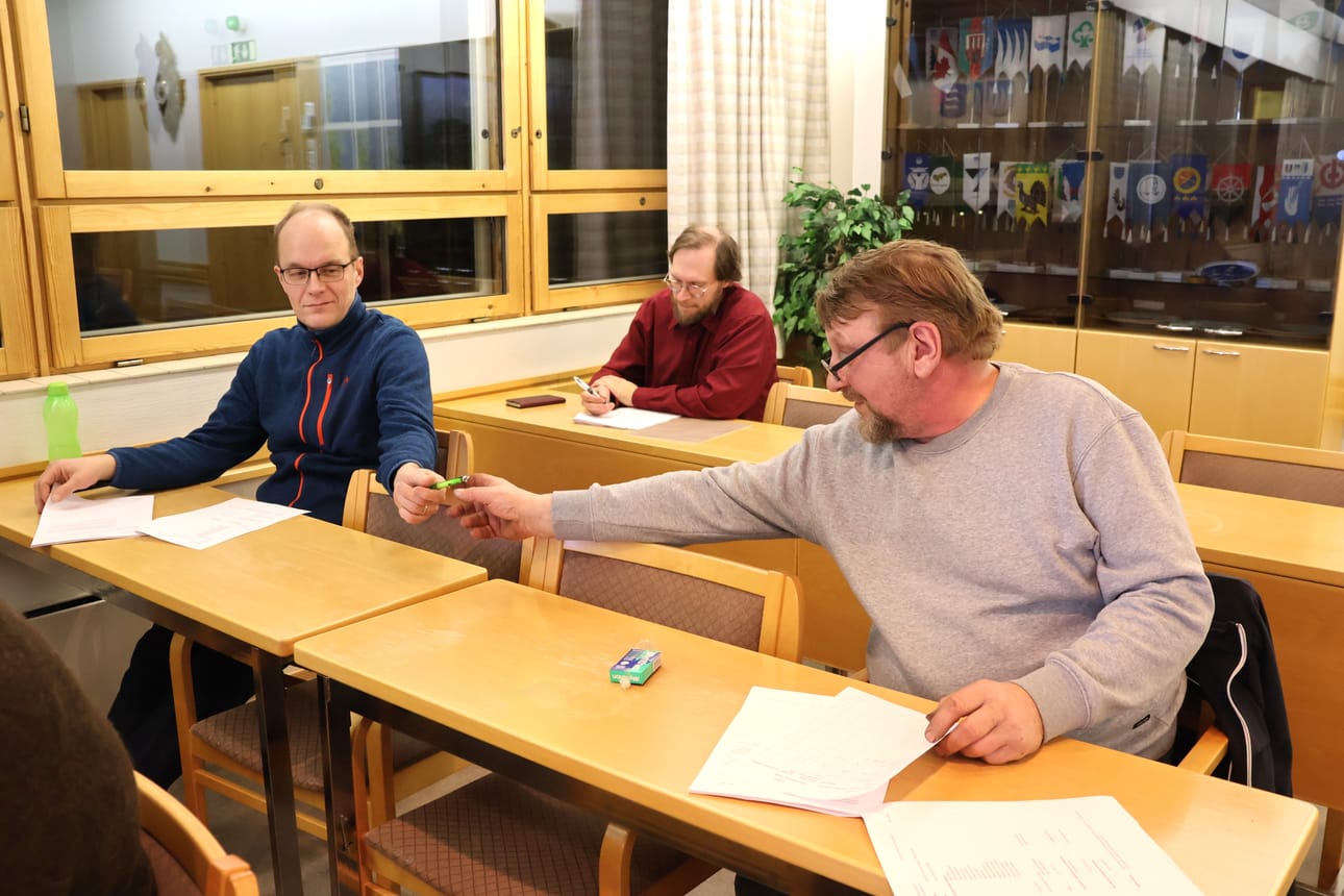 Karijoen kunnanvaltuusto kokoontui maanantaina. Mikko Savolainen ojentaa kynää Jari Malmille (oik.). Heidän takanaan istuu varavaltuutettu Petri Ahola. He ovat keskustan ryhmän valtuutettuja.