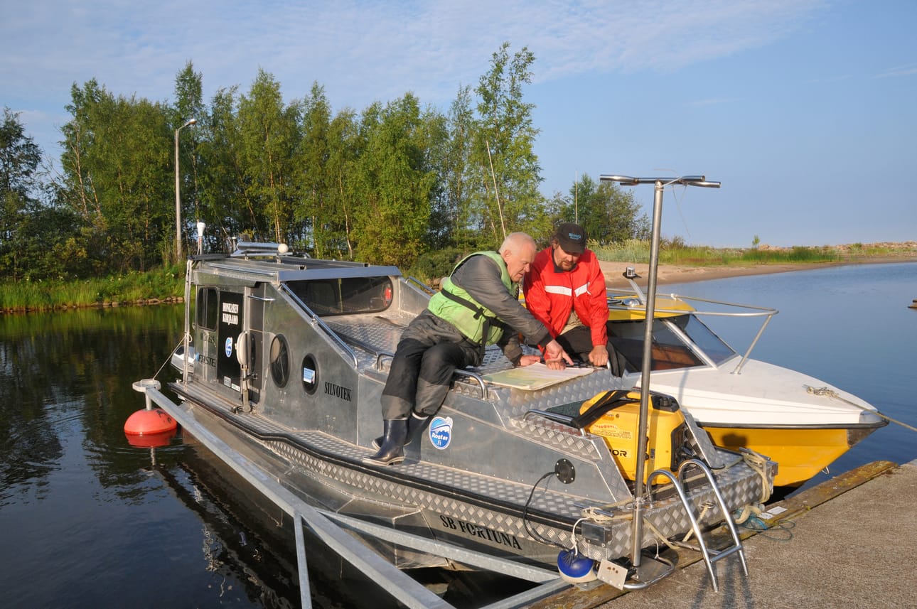 Reino Savukoski ja Timo Taari suunnittelemassa etsintäreittejä Savukosken erikoisvalmisteisen veneen kannalla Tauvon venesatamassa. Kuvat: Timo Taari