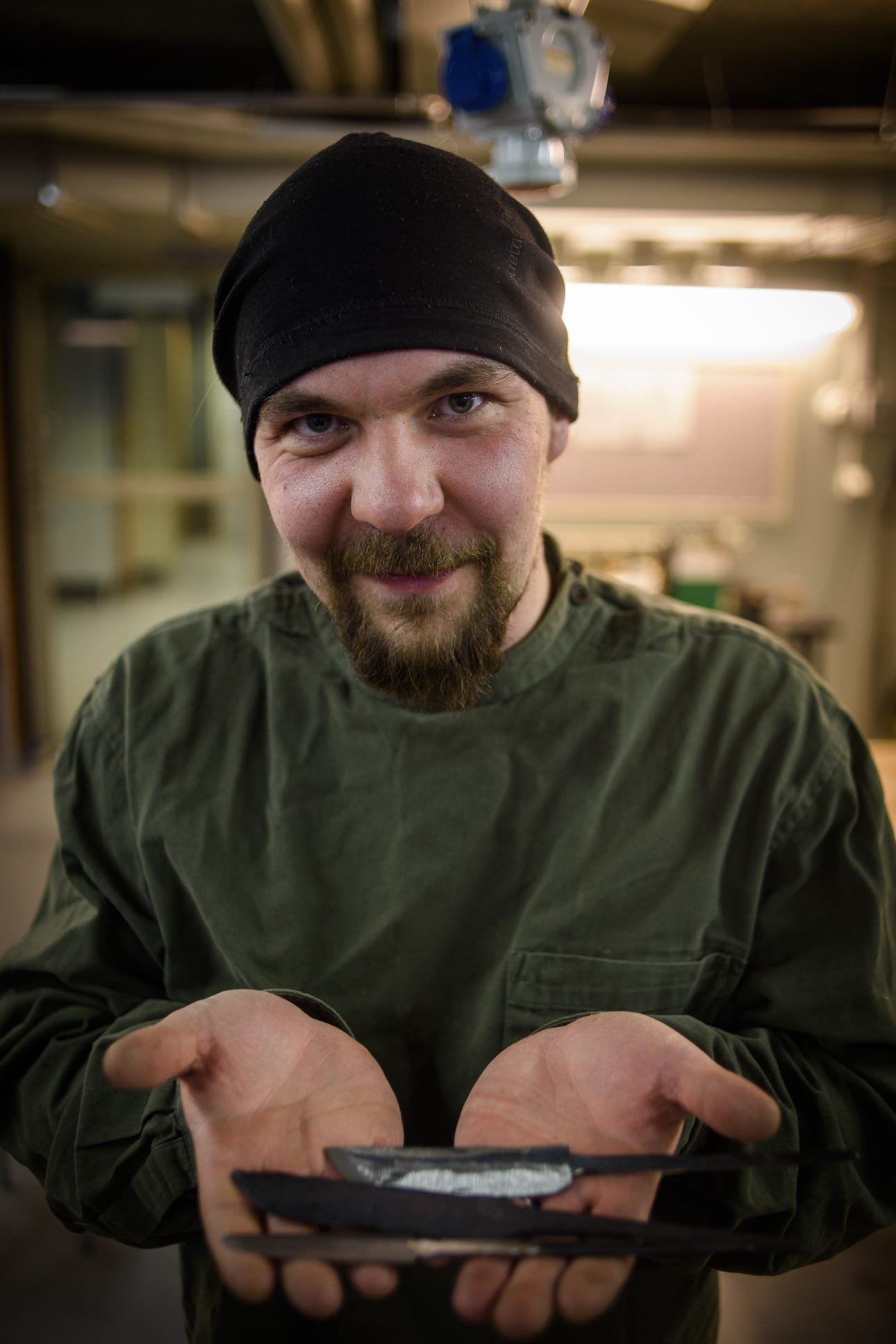 Iiro Hoikkala pitää kädessään takomiaan teriä, jotka muotoutuvat pikku hiljaa valmiiksi puukoiksi.