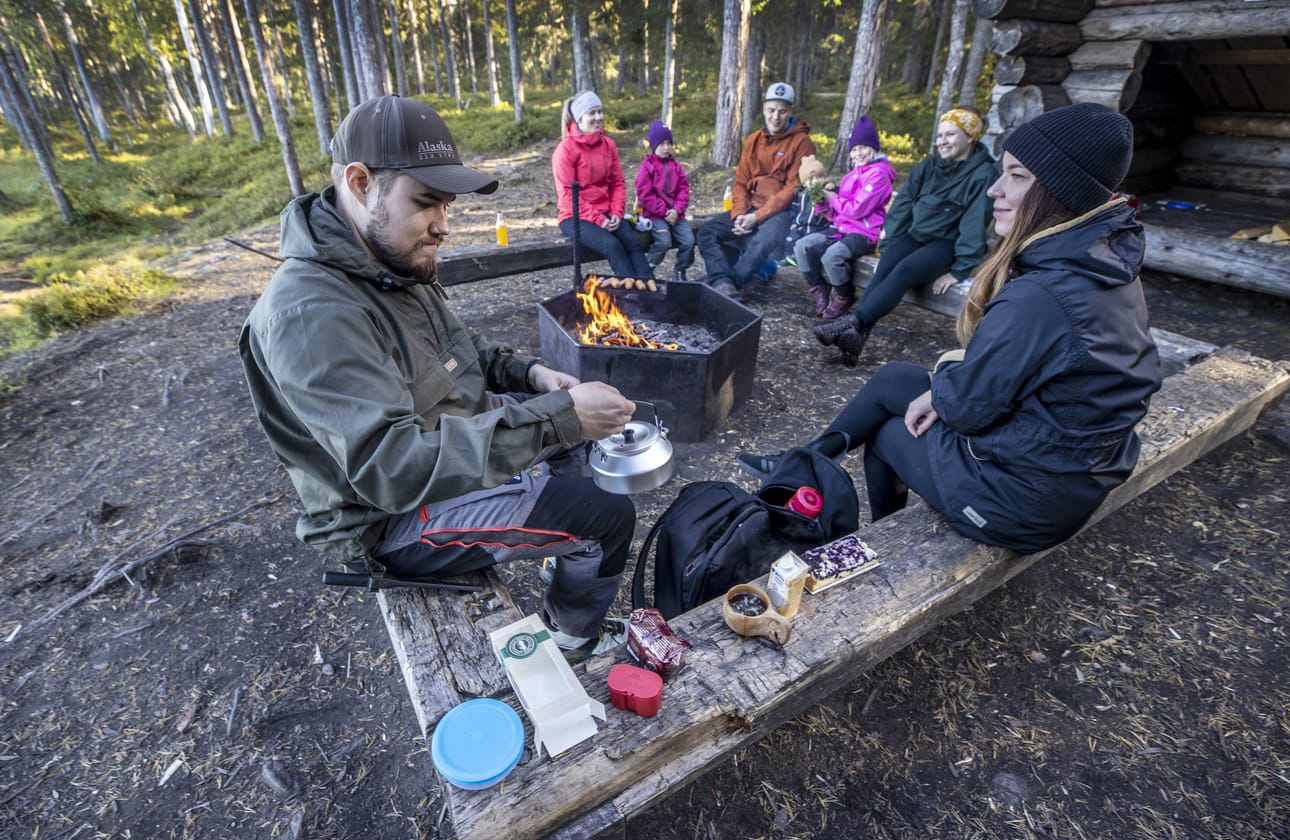 Marko Luukkonen kaataa itselleen ja Iina Kemille nokipannukahvia Isokankaan laavulla. Taustalla (vas.) Hanna-Leena ja Eevi Kyllönen, Juho, Kaarlo, Venla ja Mirja Korkala. Seurueet kertovat olleensa aktiivisia retkeilijöitä jo ennen koronan luontobuumia.