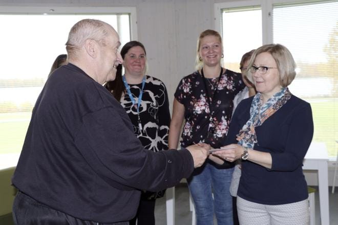 Alajärven Rantakotiin syyskuun alkupuolella muuttanut Reijo Lepistö ojensi Eeva Marjamäelle palkinnon voittaneen nimiehdotuksen ansiosta. Tapahtumaa seuraamassa henkilökuntaa. KUVA: SARI HEINILÄ