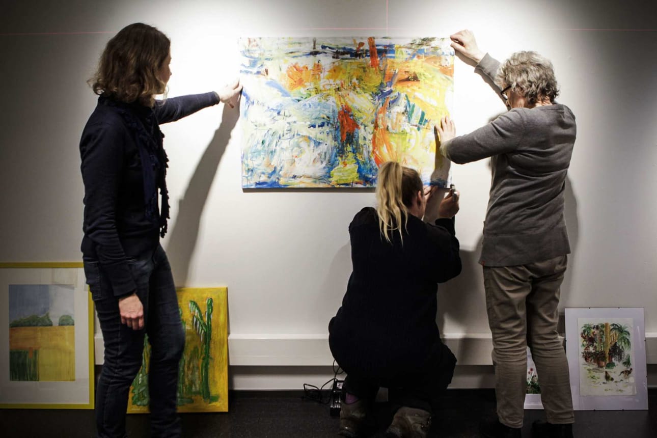 Elina Temmes, Liisa Tiihonen ja Marja-Leena Hyvärinen mallaavat teosta seinälle.