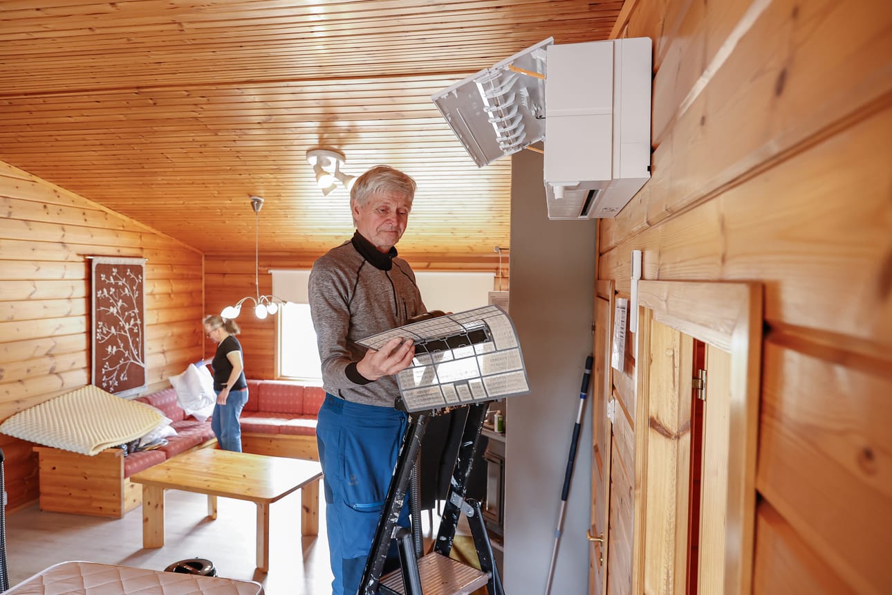 Ilmalämppöpumpun sisäyksikon suodatin on hyvä puhdistaa imurilla tasaisin väliajoin. Onni Heikkala imuroimassa suodatinta, taustalla Raija Heikkala kasaa petivaatteita puhdistettavaksi.