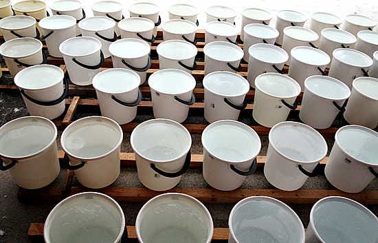 Pakkassäällä Paakinmäen talojen pihoilla on vieri vieressä kymmenen litran sankkoja täynnä vettä.