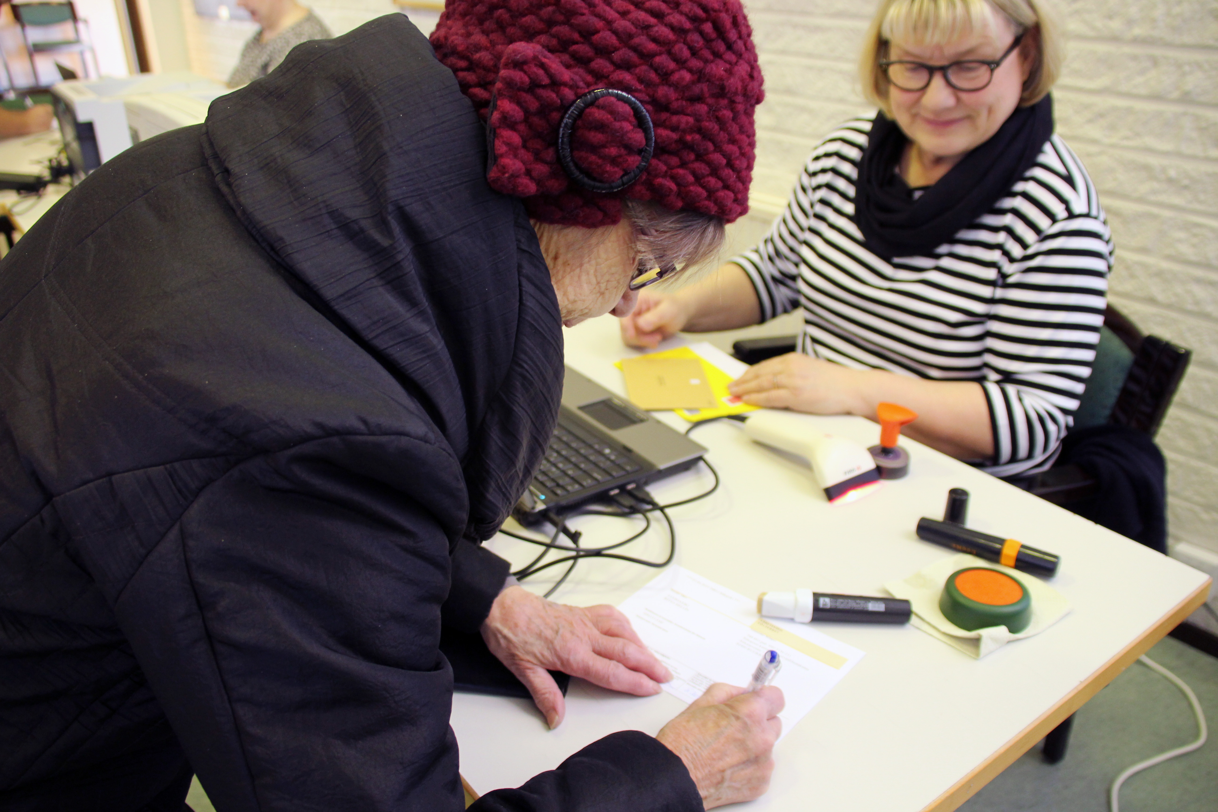 Ritva Luomajoki allekirjoittaa ennakkoäänestyksen lähetekirjettä. Taustalla vaalivirkailija Taina Stoor.