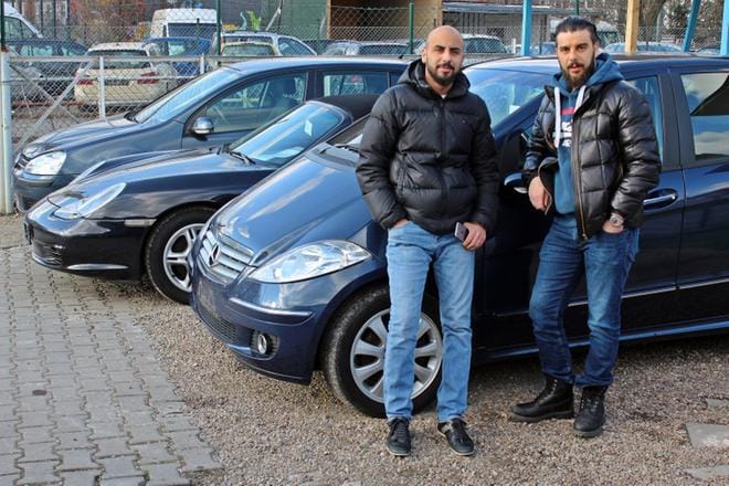 Käytettyjen autojen kauppiaat Kaiser Azam (oik.) ja Ibrahim Azam nojaavat hiljaiseksi muuttuneen kauppansa pihalla dieselautoon, joka uusimpia päästönormeja täyttämättömänä voi joutua pian ajokieltoon. Kuva: Visa Noronen