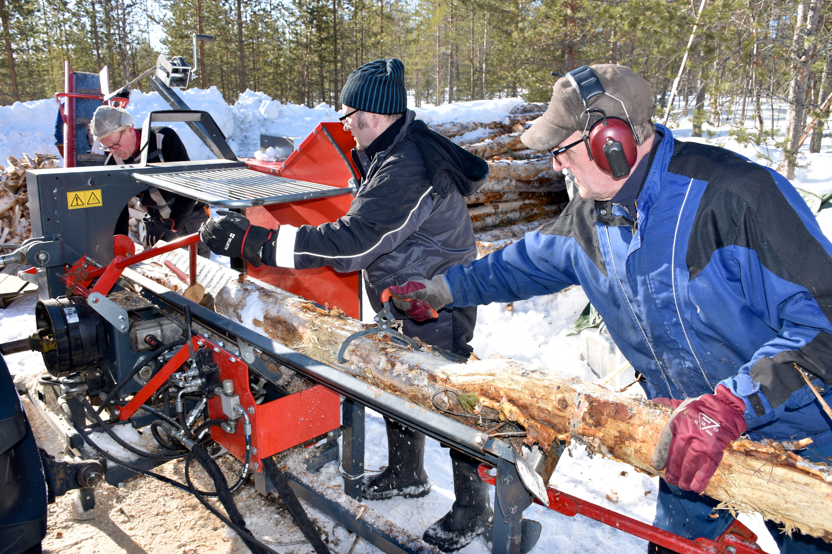 Talkoomiehet Mauno Reinikka (vas.), Heino Kulojärvi ja Eero Laine työntävät koivurankaa halkomakoneeseen.