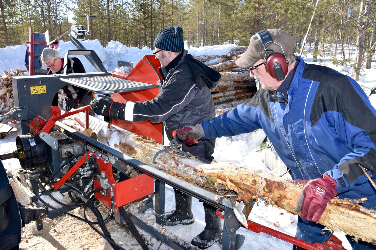 Talkoomiehet Mauno Reinikka (vas.), Heino Kulojärvi ja Eero Laine työntävät koivurankaa halkomakoneeseen.
