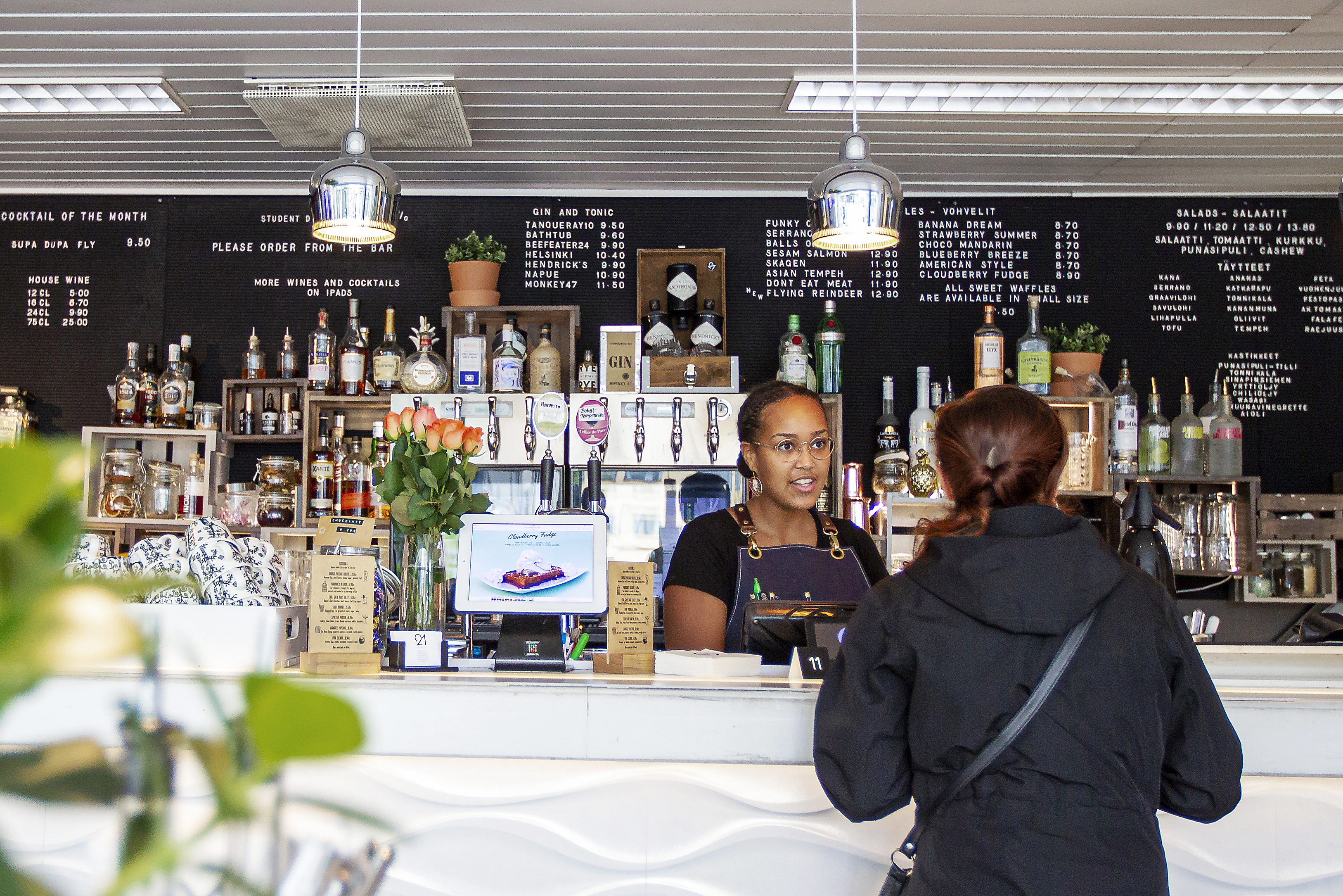 Cocktail-baarina aloittaneen Cafe & Bar 21:n listalta löytyy nykyään myös vohveleita, salaatteja ja jäätelöitä. Sisustuksessa on moderni ote ja vaikutteita maailmalta. Kuvassa tiskin takana asiakasta palvelee Rosa Costa.