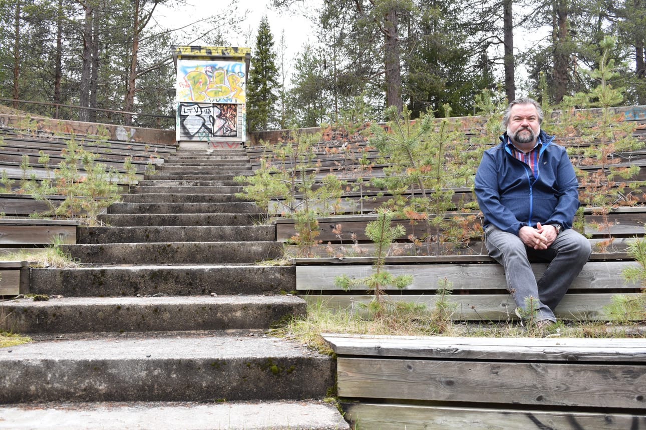 Kuusamon Näyttämön puheenjohtaja Harri Laurila istuu Helilammen vanhan kesäteatterialueen katsomossa, jossa kasvaa jo mäntyjä. Alueen rakennukset ja katsomo ovat osin huonokuntoisia.