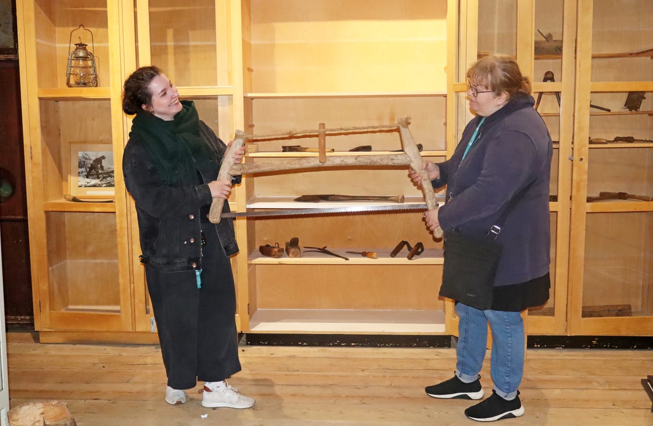 Pudasjärven kulttuurisuunnittelija Henna Hiltunen ja museonhoitaja Maria Laakko testaavat kotiseutumuseon esineistöön kuuluvaa pokasahaa.
