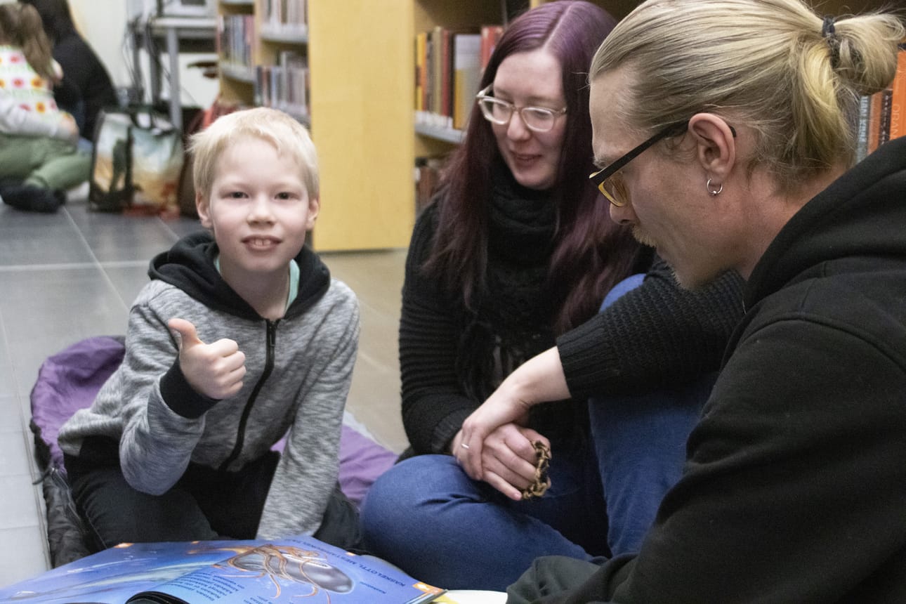 Anna ja Jarkko Pekkala tutustuivat poikansa Ronin johdolla hyvin kirjastoyöhön sopivaan kirjaa Merten elämää, jossa ääriviivat alkavat hohtaa valossa. Iltasatuhetki oli mukavaa yhdessä oloa.