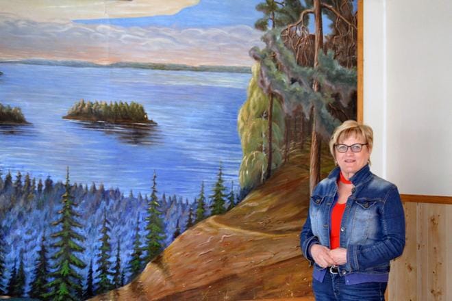 Arja Miettinen esittelee Palosaaren työväentalon kahvilaa koristavaa kookasta maalausta, jonka on tehnyt palosaarelainen Toivo Kamila. Kuva: Sara Isosomppi