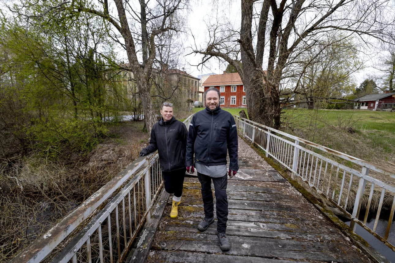 Lakkitehtaan uudet omistajat Päivi Hakkarainen ja Juha Ollila Nenättömänluoman ylittävällä sillalla. Taustalla näkyvän tehtaanpuiston takaa siintävät alueen teollisuusrakennukset. Pariskunnan tavoitteena on elävöittää yritystoiminnan avulla historiallisesti merkittävä alue rakennuksineen uuteen aikaan vanhaa vaalien.