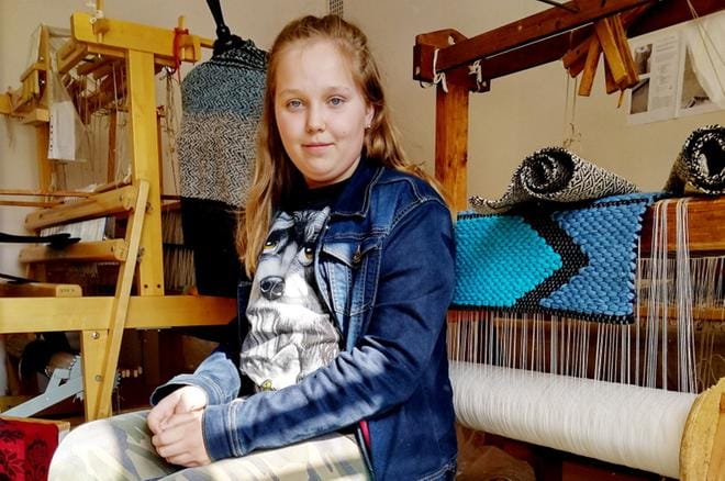 Sääksjärven kutojien nuorin tekijä Minttu Ahvenkoski istuu omin käsin tekemänsä räsymaton päällä. KUVAT: MIIANELLA HERRALA