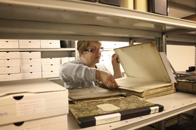 Kanslisti Taina Hallapuro etsii arkiston vanhimman aarteen: kirkonkirjan vuodelta 1841. Kellarin ilma on tympeää hengitettävää. KUVA: JOHANNA KATAJA