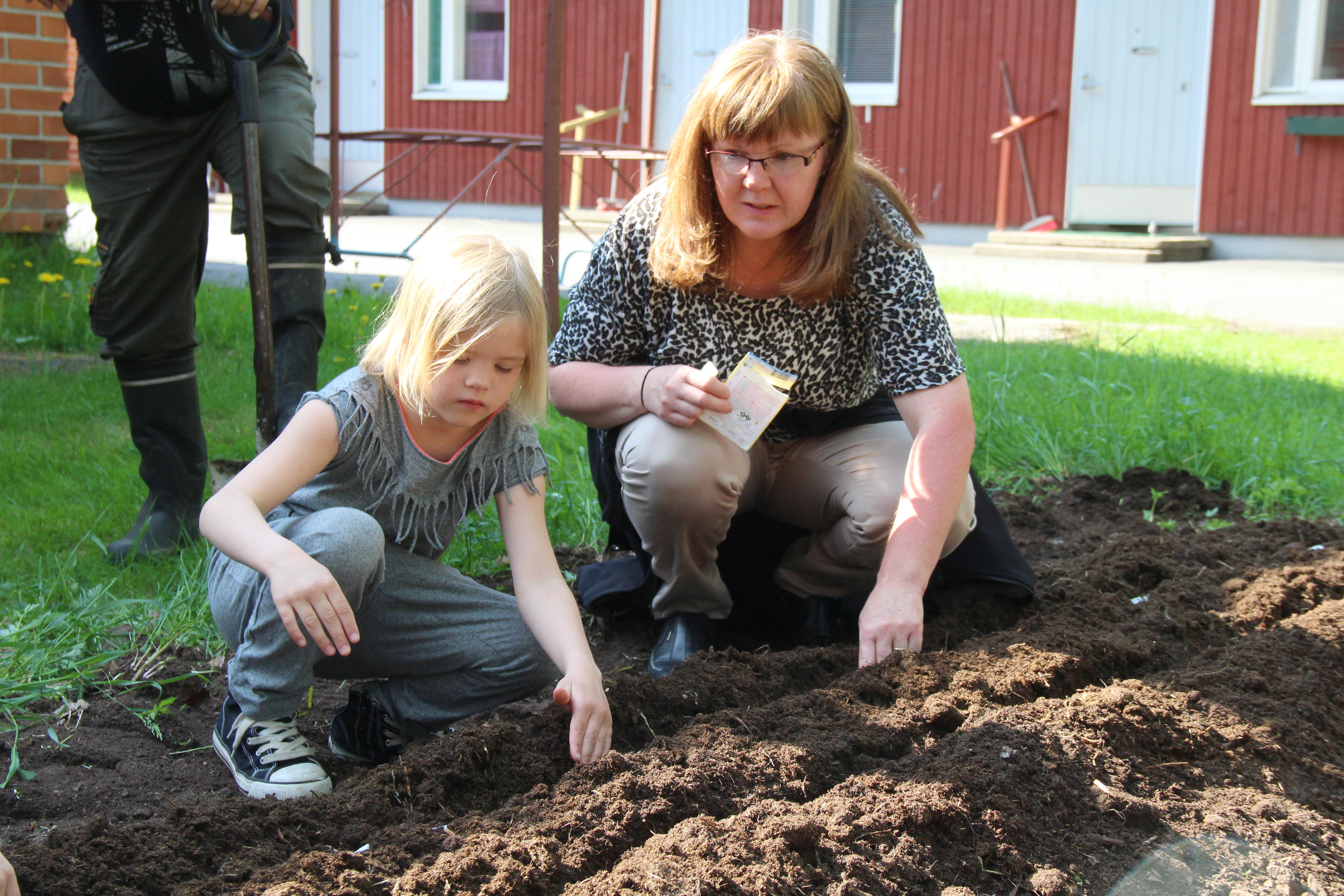 Koulunkäynnin ohjaaja Eevi Kyngäs opastaa Miila Puomiselle porkkanan istuttamisen saloja.