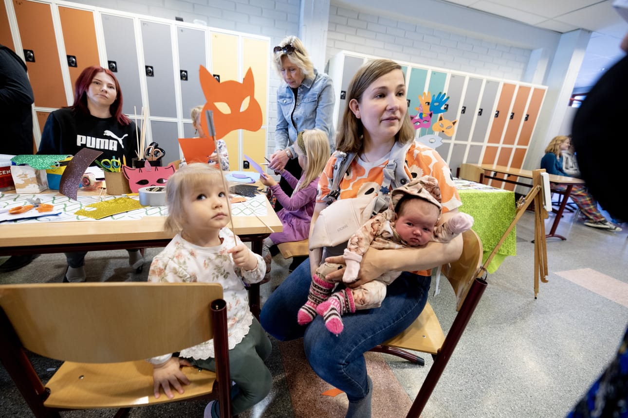Leikkipäivän askartelunurkkauksessa Siiri, 3, esittelee askartelemaansa naamaria. Äidin, Anne Hautalan, sylistä kurkistelee juuri päiväuniltaan herännyt kuukauden vanha Kerttu.