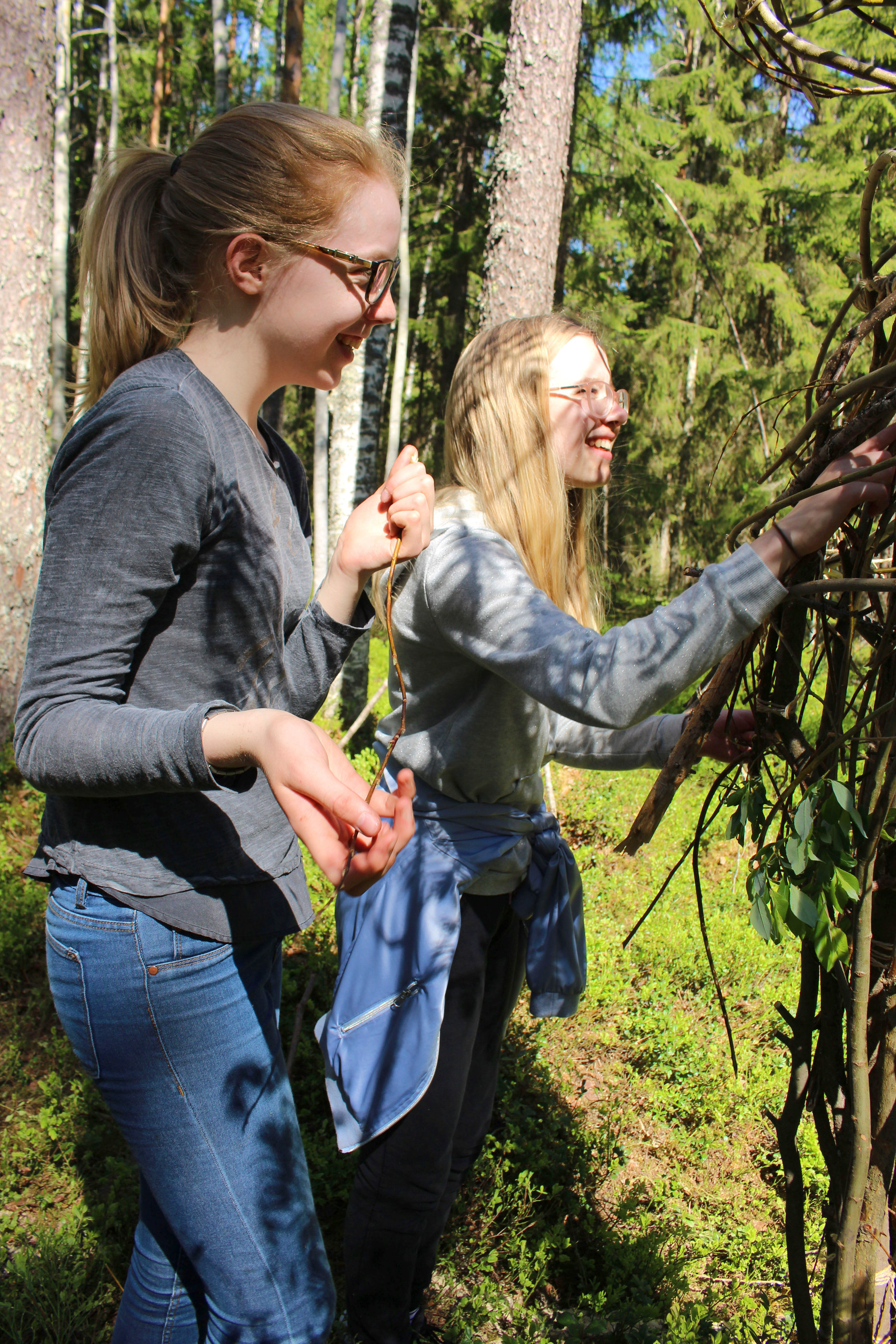 Anni Mällinen ja Sanni Vääräniemi nauttivat tekemisen riemusta, kun pääsivät punomaan puu-ukkoon oksia.