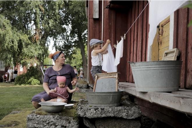 Väinö Järviö kokeilee, kuinka ennen pestiin pyykkiä. Vierestä pyykinpesua talon portailta seurailee Pia Järviö ja Inkeri Järviö. KUVAT: HANNU TOIVONEN