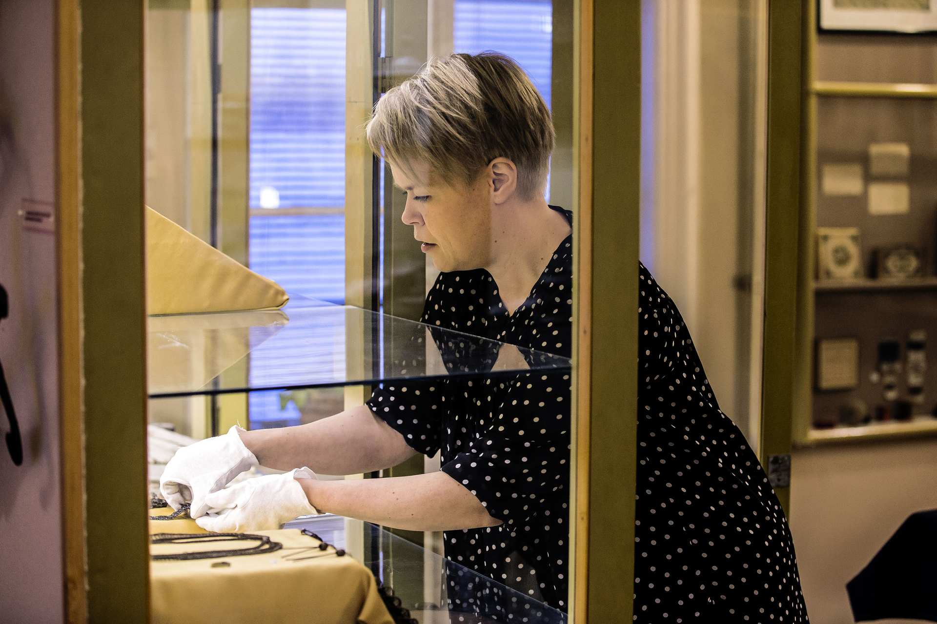 Anna Latomaa tyhjentää vitriiniä hellävaroen, että pääsee pyyhkimään lasihyllyn pölystä. –Vanhojen esineiden siirtely jännittää aina, Anna sanoo.