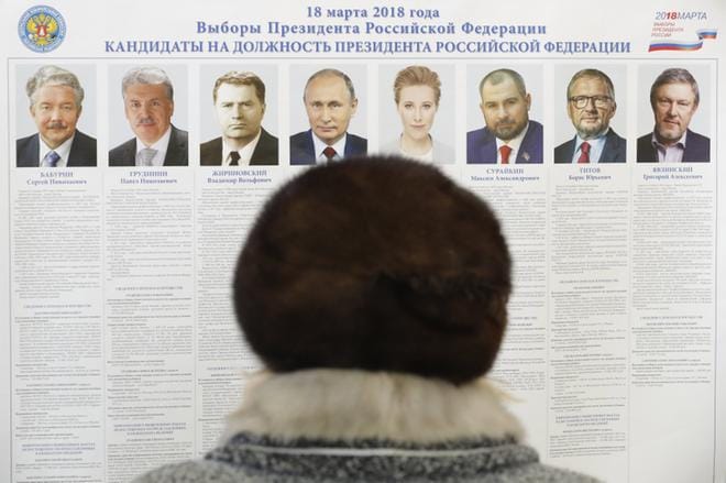 Nainen katselee ehdokasesittelyä Leninin sovhoosi -nimisellä äänestyspaikalla Moskovan ulkopuolella. Ehdokkaita on kahdeksan, mutta Vladimir Putin on heistä ainoa useimpien tuntema poliitikko. EPA: Sergei Ilnitsky