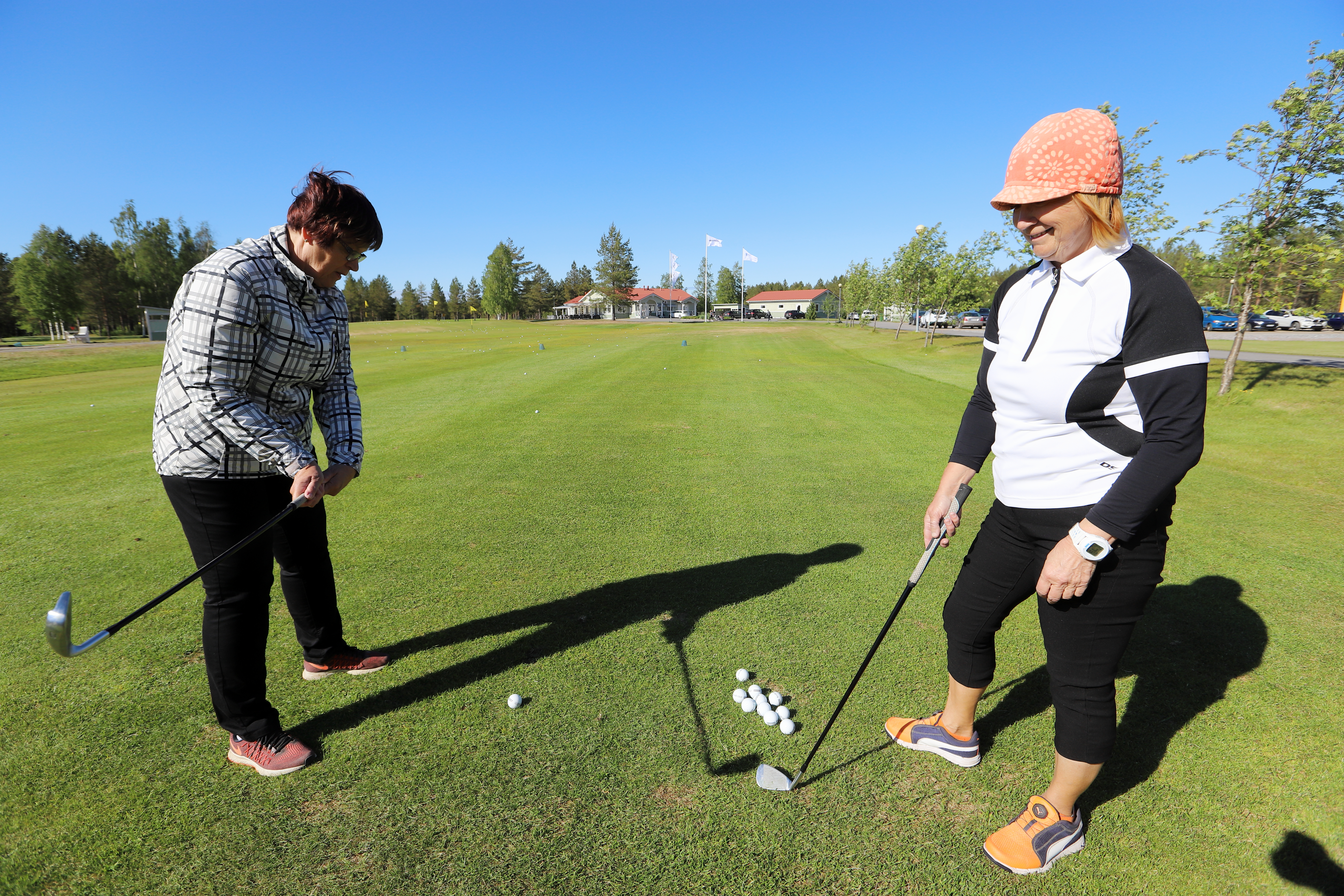 Kymmenen vuotta golfannut Heli Juusola opastaa Hilkka Katajamäkeä oikean lyöntitekniikan löytymisessä.