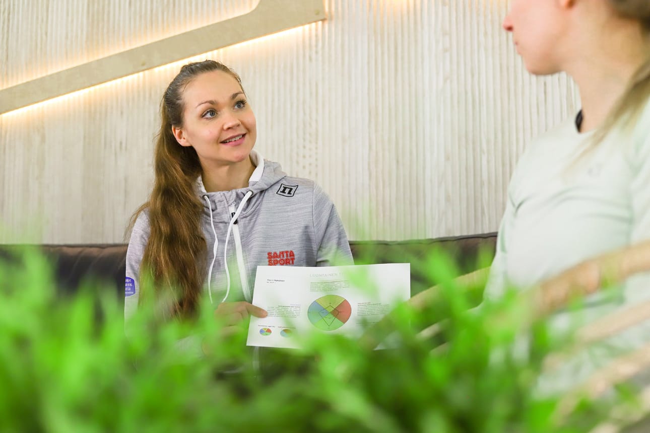 Santasportin hyvinvointivalmentaja Mari Ulkuniemi esittelee asiakkaalleen hyvinvointinavigaattoria, joka on oivallinen työkalu parhaan polun löytämiseksi kohti hyvinvointia.
