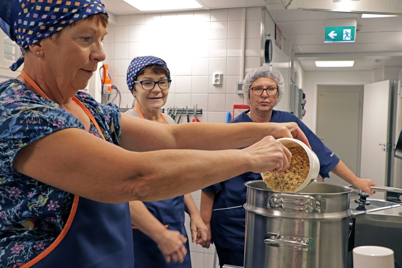Anna-Maija Rahja lisää maitoon valmiiksi liotetut kauraryynit. Taustalla Armi Nikola ja Siikapirtin keittiön Sirpa Utunen.