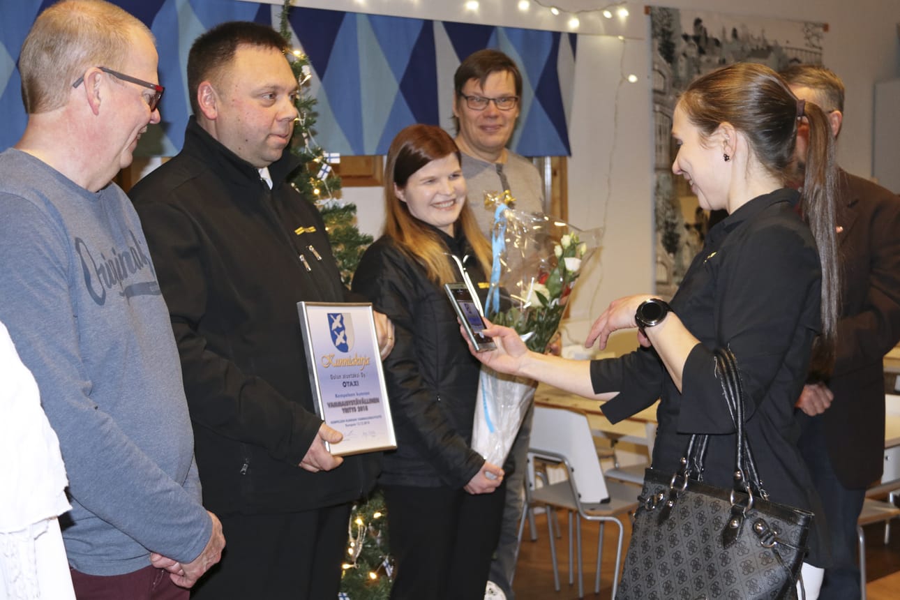 Piia Sandholm ikuisti Juha Hietaharjun pitelemän kunniakirjan. Vieressä hymyilee Katri Holma. Vasemmalla vammaisneuvostoa edustaneet Raimo Tikkanen ja oikealla Timo Niemelä.