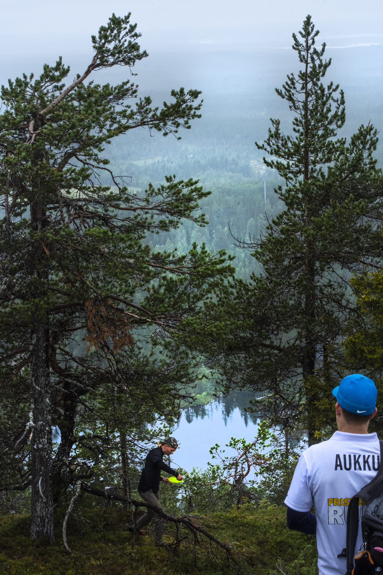 Eetu Parkkisenniemi heittää frisbeetä Rukan päällä.Uusi ilmainen ammattilaistason rata siirtyy frisbeegolfseuran ylläpidettäväksi. Etualalla Markus Määttä katsoo heittäjää maisemassa.