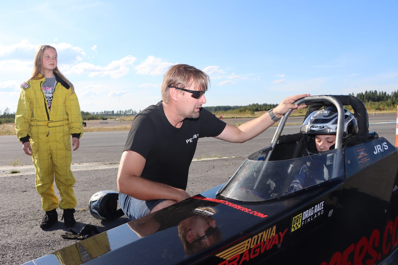 Pinja Junnila seuraa taustalla, kun hänen isänsä Ilkka Junnila opastaa ensimmäistä kertaa puikoissa istuvaa Julia Tikkaojaa Junior Dragsterin käytöstä.