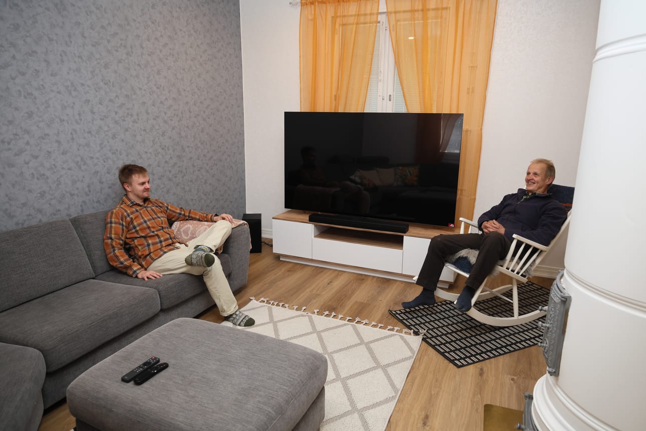 Tässä tilassa oli aiemmin toimisto, mutta nyt siitä on muokattu olohuone Valtteri Pelkoselle (vas.). Pönttöuuni on alkuperäinen, mutta sen toimivuutta ei ole vielä testattu. – Kyllä sen pitäisi ihan käyttökelpoinen olla, Reijo Pelkonen (oik.) tuumaa.