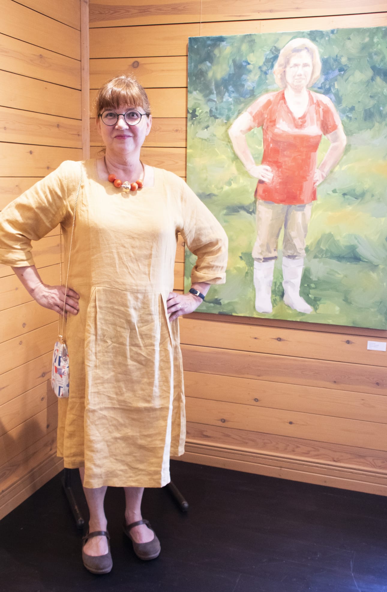 Helena Helisten poseeraan Nokialaiset-nimeä kantavan omakuva öljyvärimaalauksen edessä. Näyttelyssä on esillä hänen mustemaalauksina tekemiä kuvia, joissa on aiheita myös vanhempien kotiseudulta Rantsilasta.