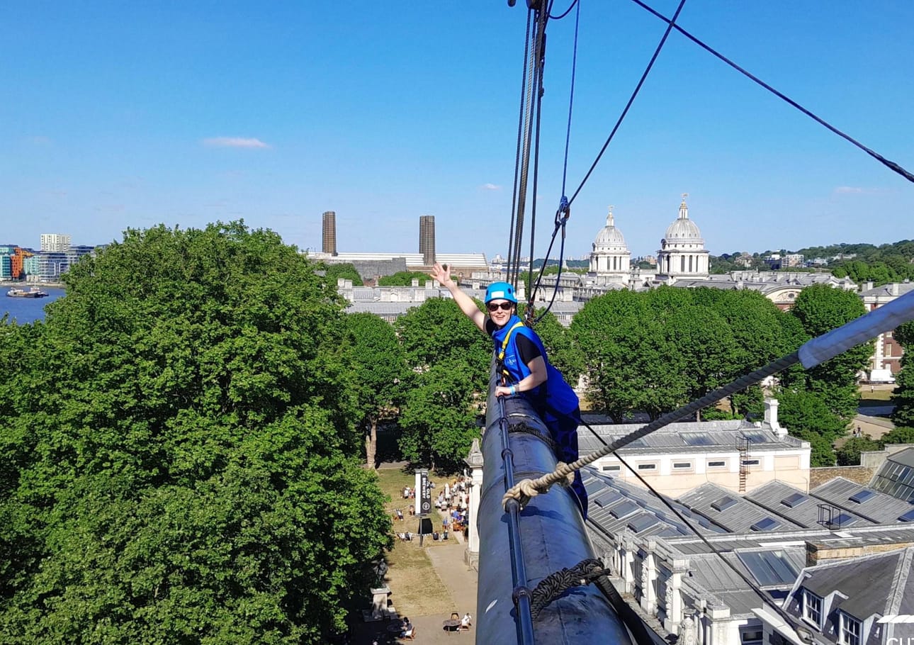 Katja Walsh kiipeilemässä Cutty Sark -laivan raakapuuta pitkin eli mistä isot purjeet roikkuvat. Takana näkyy Greenwichin Old Royal Naval College kupolit. Kaksi savupiippua kuuluvat varavoimalaitokselle, Greenwich Power Station, joka toimii Lontoon metron varavirtalähteenä.